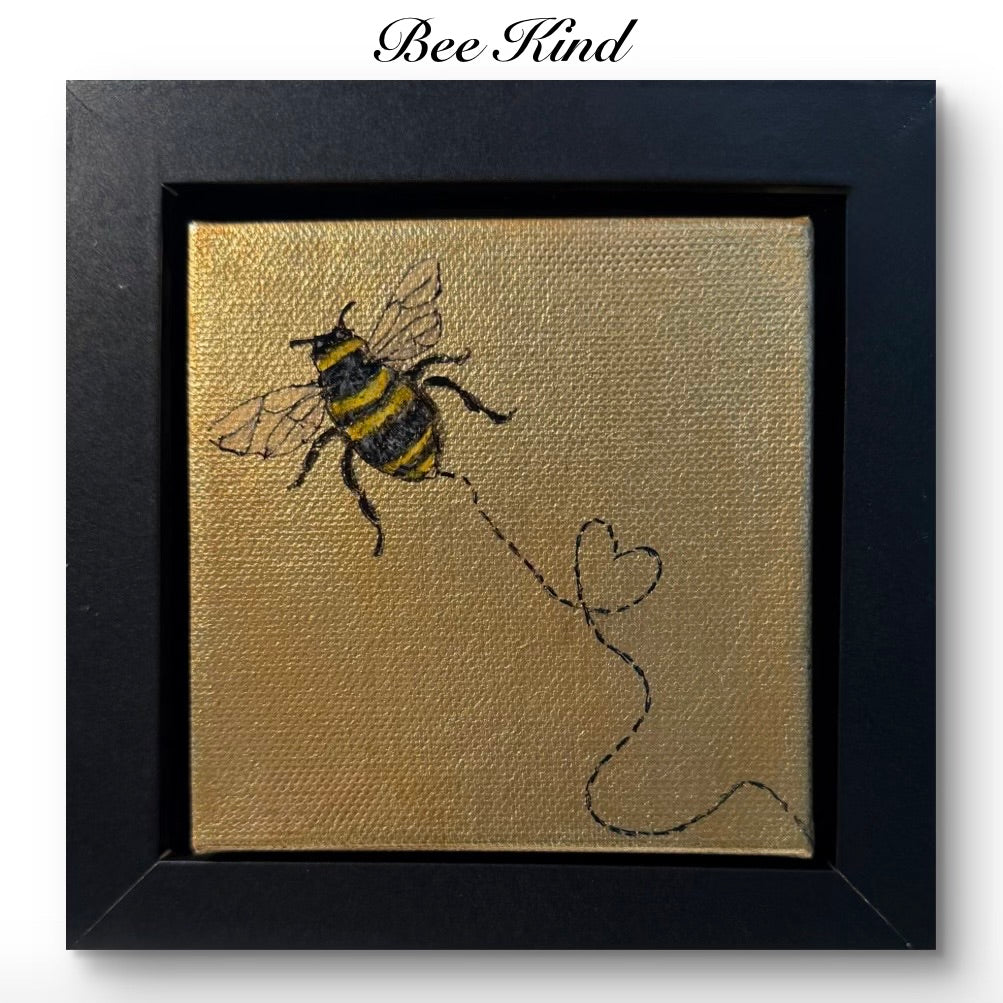 Framed original artwork of a bee with a heart trail on gold leaf, labeled 'Bee Kind'.